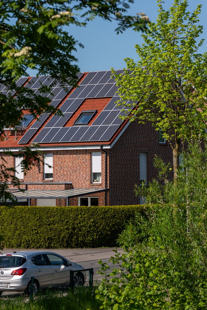 gallery-02 A modern brick house with solar panels on the roof, surrounded by lush greenery, under a clear blue sky.